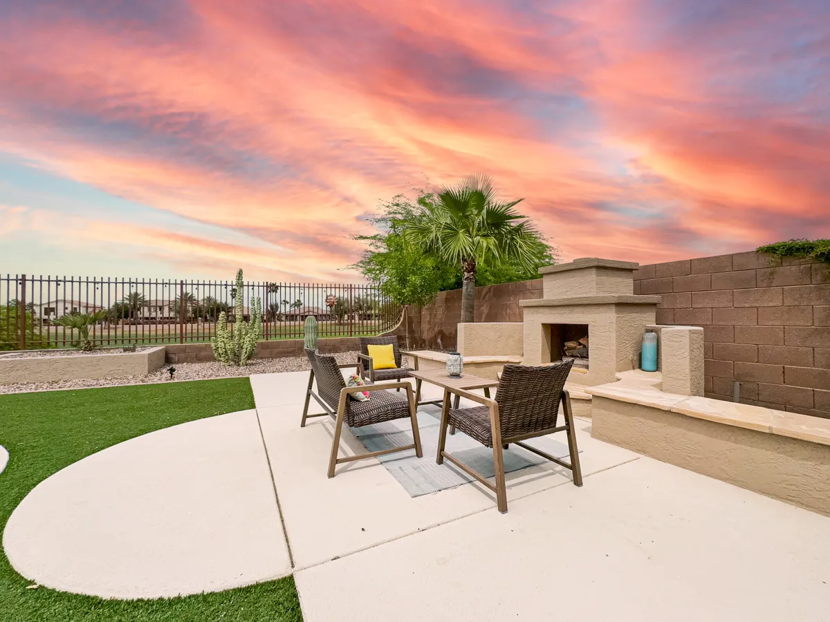 An inviting outdoor seating area with a cozy fireplace, surrounded by beautiful landscaping and set under a vibrant sunset sky. The scene suggests evening gatherings, stargazing, and a tranquil lifestyle that extends past daylight hours.