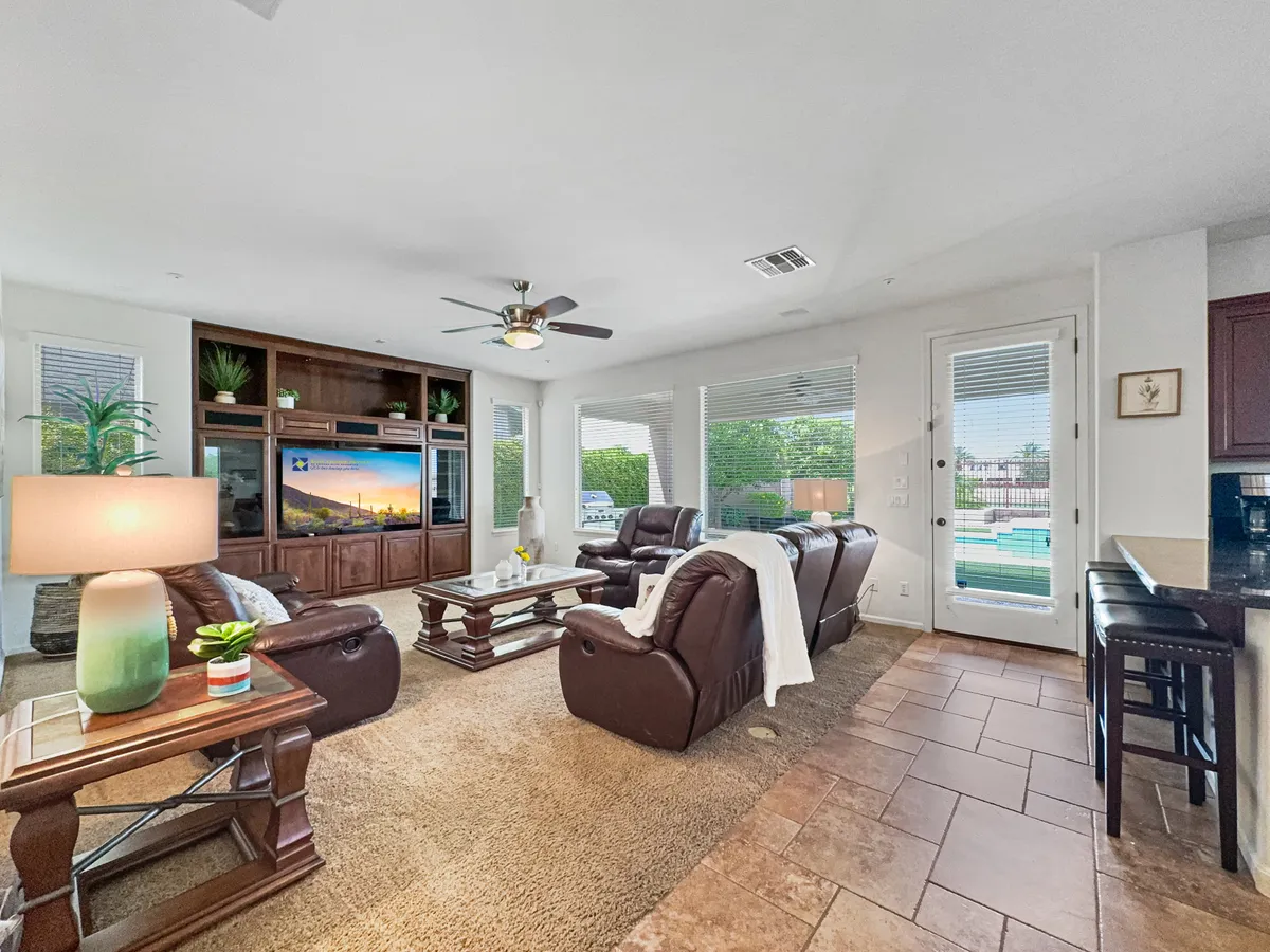 This inviting interior photo showcases a comfortable living area with leather sofas, a large entertainment unit with a massive TV, and glass doors that open directly to the outdoor pool area. The space is designed for socializing, movie nights, or simply lounging with friends and family.