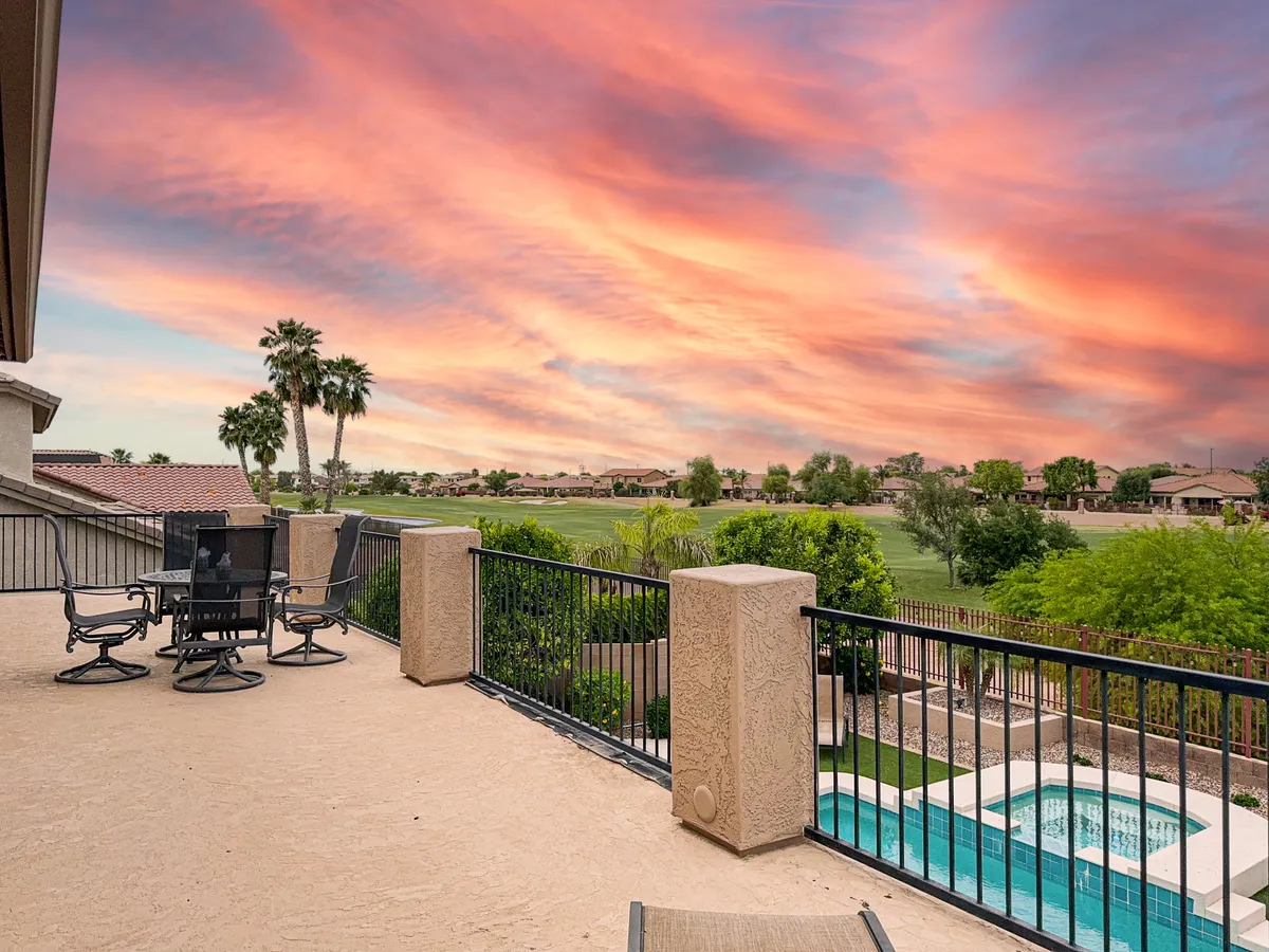 A tranquil exterior shot showcasing a balcony seating area overlooking a pristine swimming pool, with a sweeping landscape and a vibrant sunset sky in the background. The setting exudes relaxation and offers a perfect vantage point for unwinding, entertaining, or simply enjoying the evening ambiance.