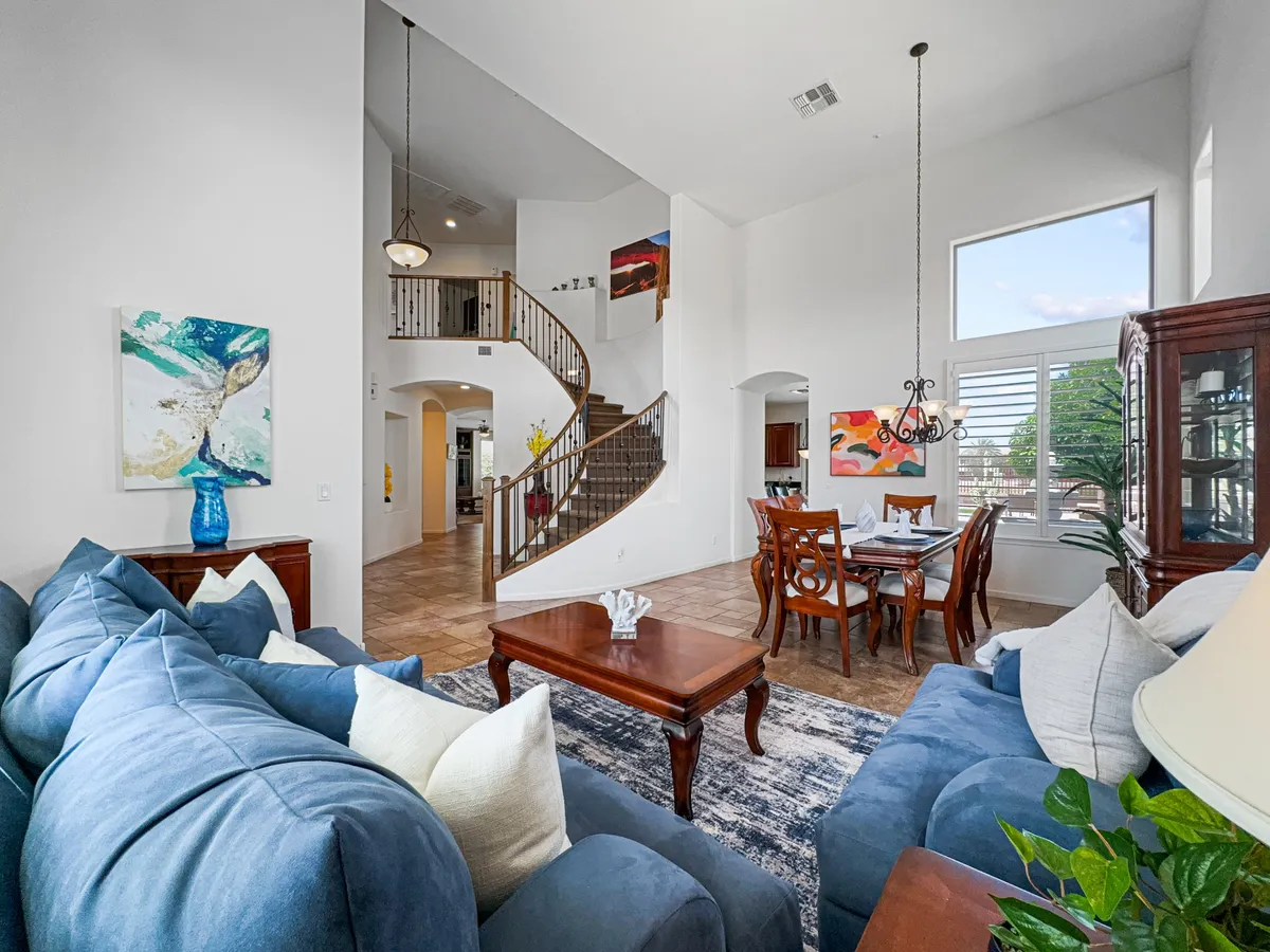 This image features an inviting open-concept space with a blue sectional sofa, a dining table set for gatherings, a striking spiral staircase, and artwork on the walls. The arrangement allows for seamless transitions between the living and dining areas, ideal for entertaining and relaxation.