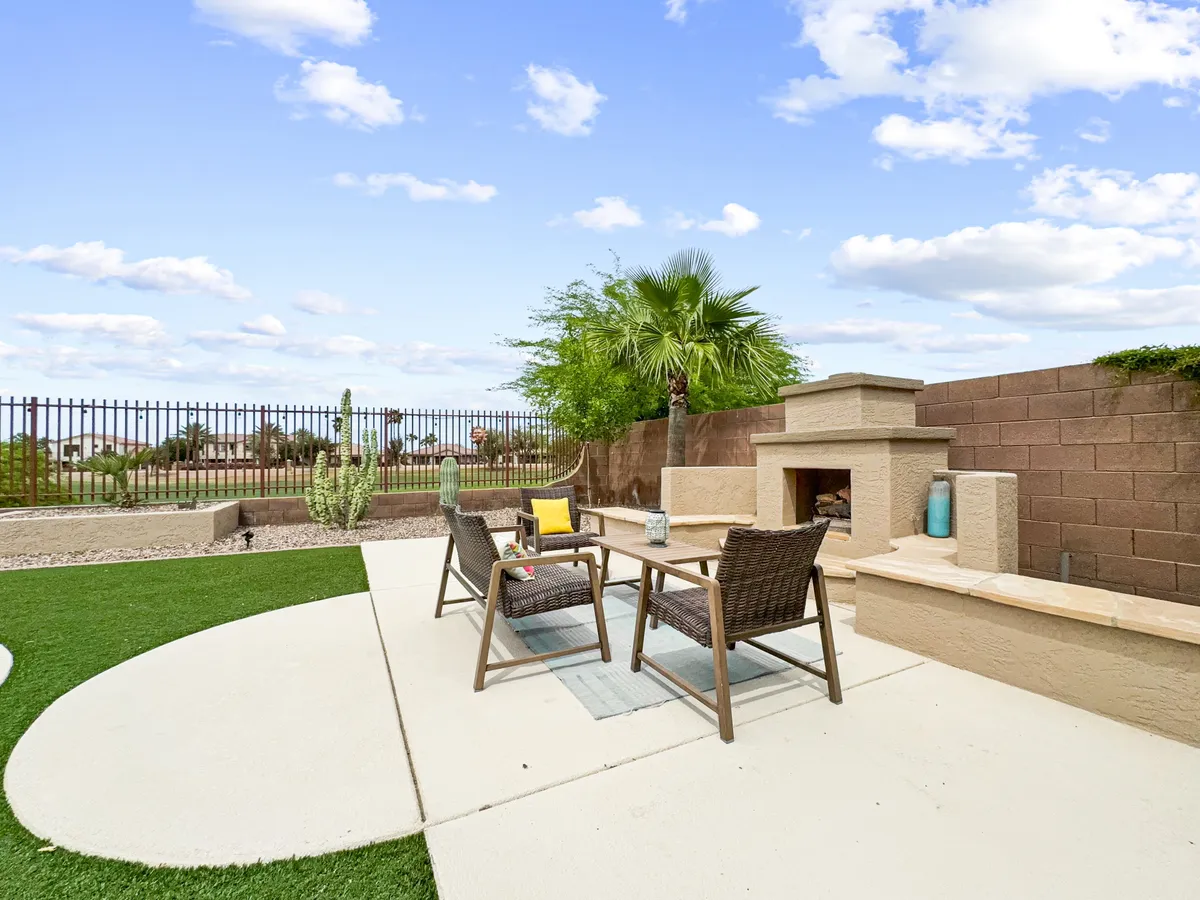 A cozy outdoor area centered around a stylish fireplace, surrounded by comfortable seating and decorative stones with a palm tree accent. The setting is tranquil, perfect for relaxing evenings or intimate gatherings under the stars.