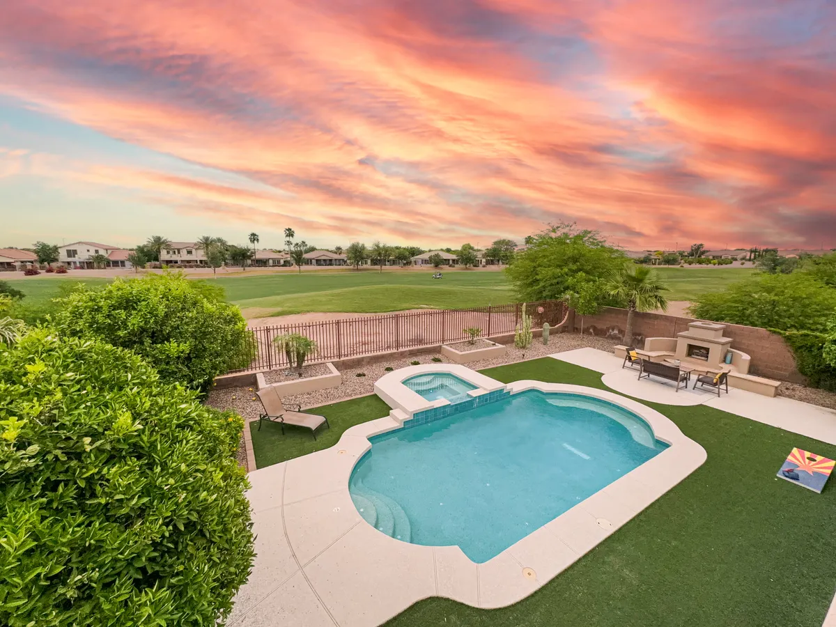 A wide-angle view of a tranquil backyard featuring a sparkling swimming pool and spa, surrounded by lush landscaping and modern outdoor seating. The sun sets in the background, casting a warm glow over the entire area, and inviting users to imagine relaxing by the water at any time of day. The space feels luxurious and private, perfect for both play and repose.