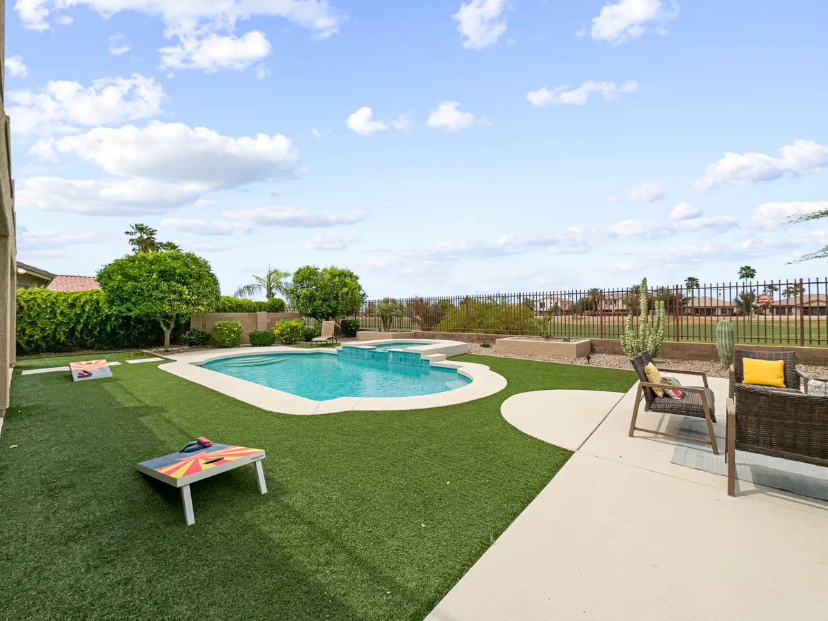 This exterior image features a sparkling swimming pool surrounded by a well-maintained lawn, outdoor seating, and bean bag toss games set up on the grass. The area is designed for relaxation and play, inviting families to gather for pool parties, sunbathing, barbecues, and game nights.