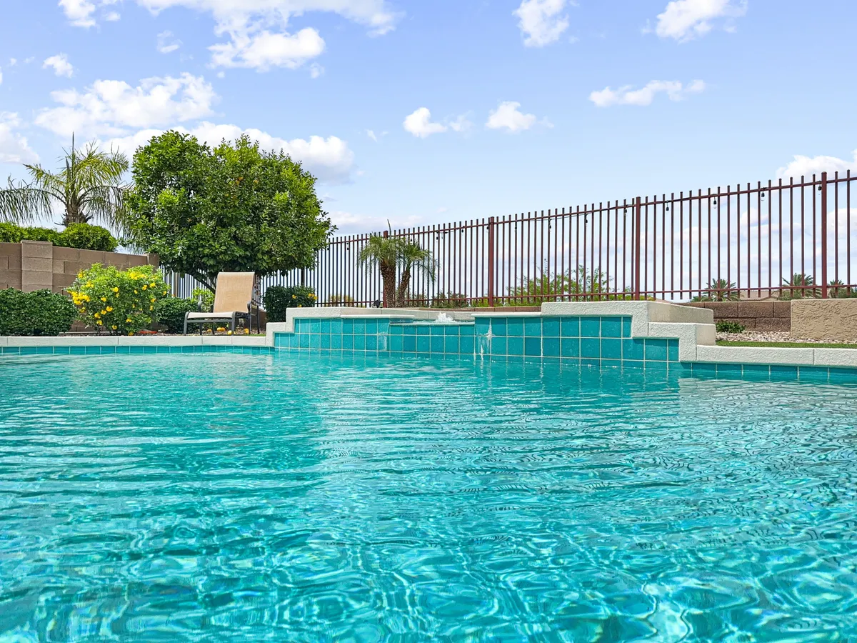A beautiful daytime exterior shot of a swimming pool bordered by a landscaped garden, lounge chairs, and privacy fencing. The inviting pool and sunny garden space evoke leisurely afternoons spent swimming, relaxing, and playing in the safety and comfort of home.